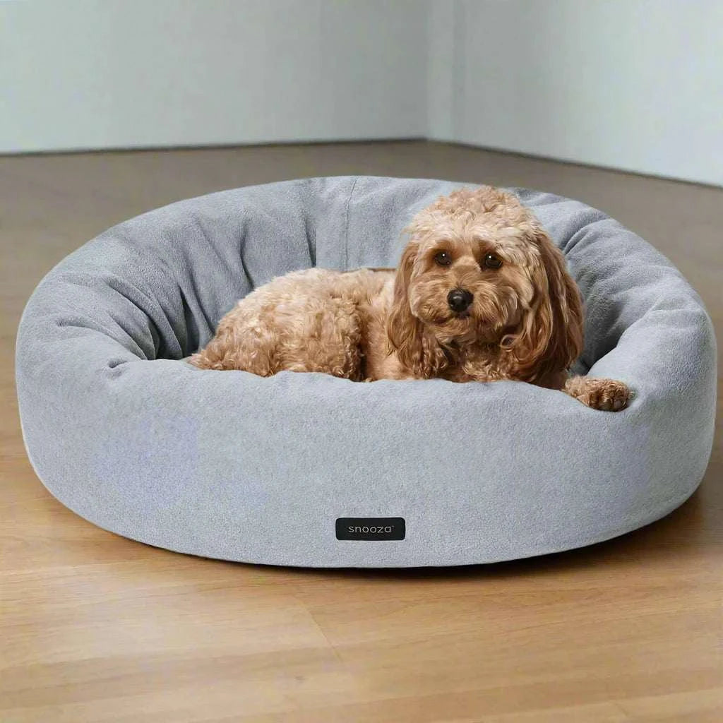 A dog sitting peacefully on a grey self-warming cuddler bed.